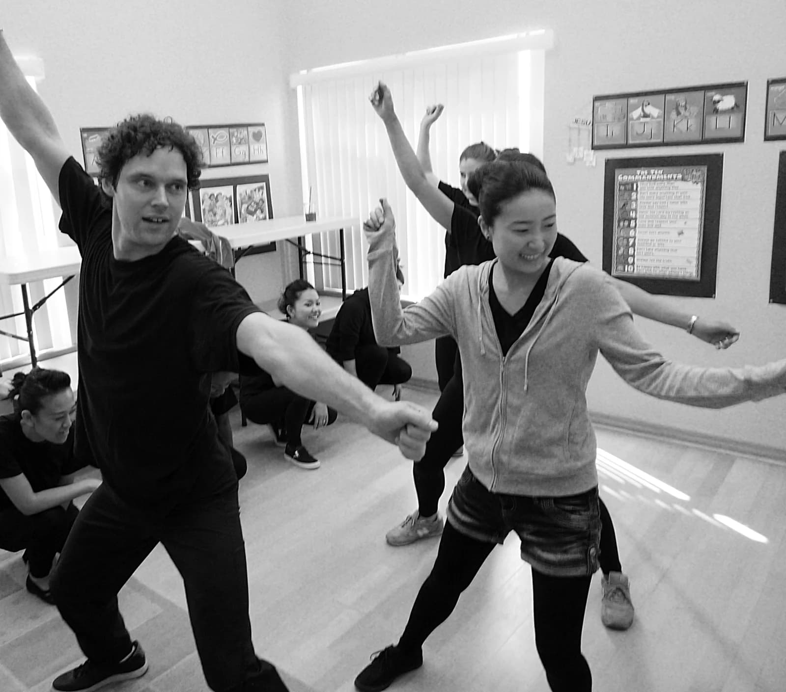 A black-and-white photograph of performers practicing coordinated movement in a rehearsal room.