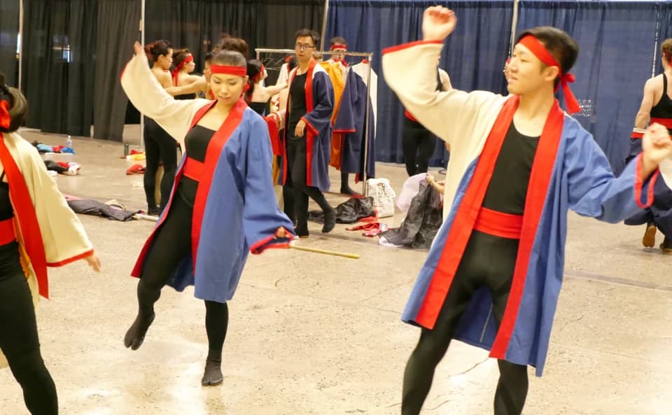 Performers in red, white and blue clothing rehearse a coordinated dance in a backstage room.