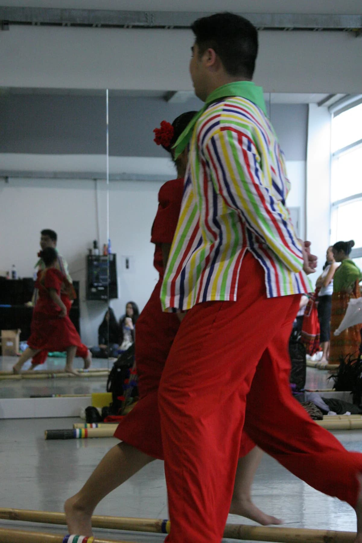 Dancers in colorful performance costumes rehearse movement together in a mirrored room.