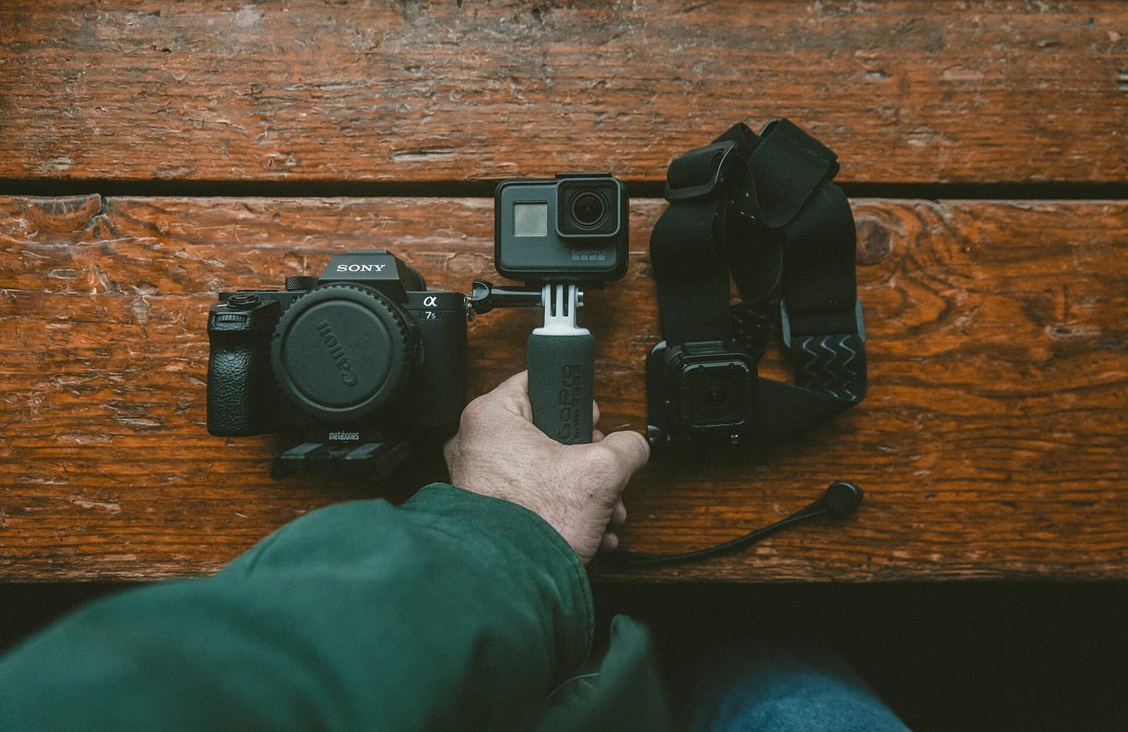 A hand selects a camera from filmmaking equipment arranged on a wooden surface.