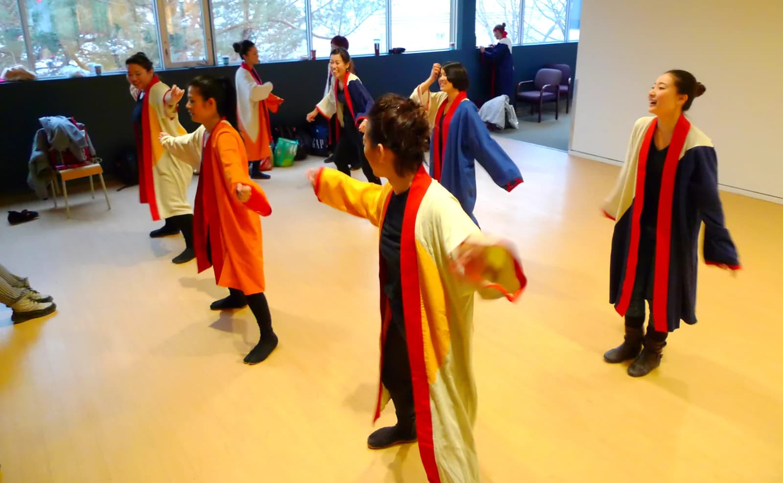 Performers rehearse movement together in bright costumes in a sunlit room.